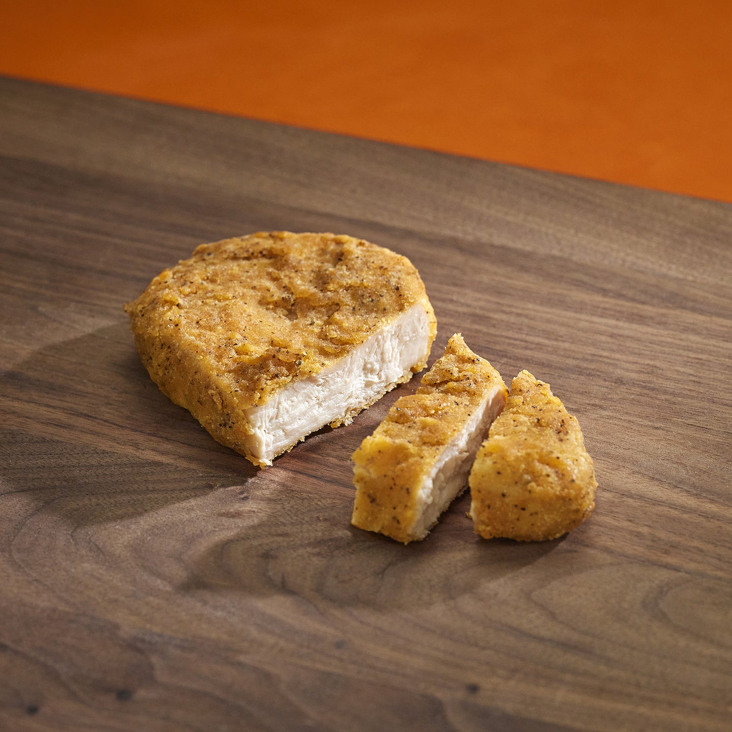 Sliced breaded chicken breast on a wooden cutting board with an orange background